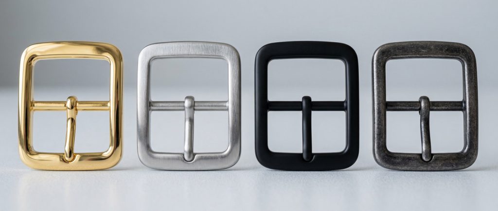 Various surface finishes for custom belt buckles including brushed stainless steel and matte black zinc alloy